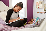 Young teen girl sitting on her bed writing in a notebook