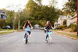 Two teen girls riding bikes in a quiet street, front view
