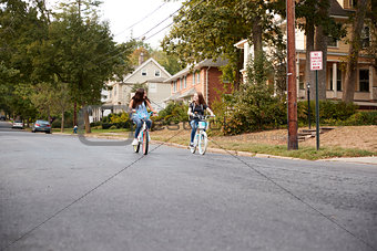 Two teen girls riding bikes in the distance in quiet street
