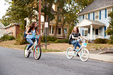 Two teen girlfriends ride past on bikes in a quiet street