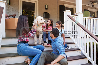Family With Dog Sitting On Steps Of New Home On Moving In Day