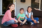 Portrait Of Children Sitting On Porch Of House Together