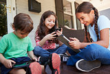 Group Of Children Sit On Porch Playing With Digital Devices
