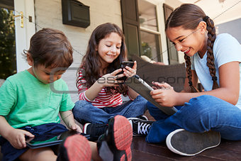 Group Of Children Sit On Porch Playing With Digital Devices