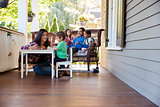 Family Sit On Porch Of House Reading Books And Playing Games