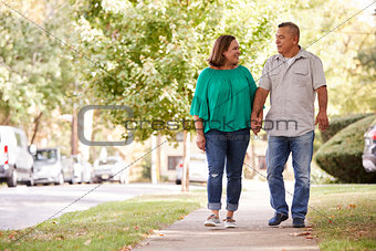 Senior Couple Walking Along Suburban Street Holding Hands
