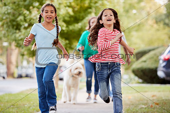 Grandmother And Granddaughters Walking Dog Along Suburban Street