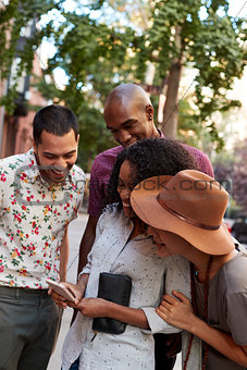 Group Of Friends In City Looking At Photo On Mobile Phone