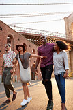 Group Of Friends Walking By Brooklyn Bridge In New York City