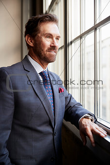 Senior white businessman looking out of window, vertical