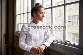 Young woman with hair bun looking out of window, waist up