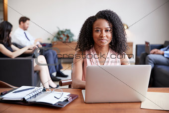 Young black businesswoman working at a desk looks to camera