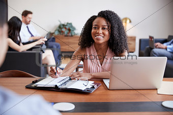 Young black woman at a desk looking to a colleague opposite