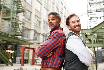 Two middle aged men stand back to back outside workplace