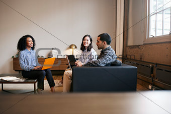 Smiling work colleagues using laptops at a casual meeting