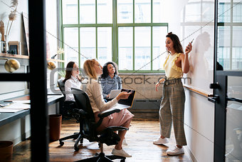 Woman pointing at whiteboard in a meeting with female team