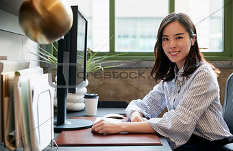 Chinese woman at a computer in an office smiling to camera