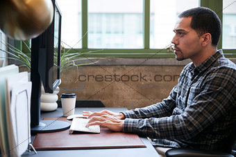 Hispanic man working at a computer in an office, side view