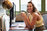 Woman sitting in an office with coffee smiling to camera