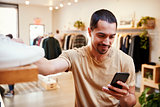 Smiling Hispanic man using smartphone in a clothes shop