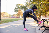 Young black woman stretching on bench in a park, full length