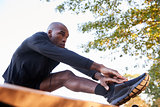 Young black man stretching leg on a bench in park, close up