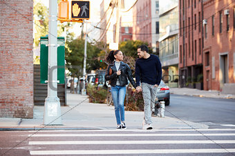 Young Hispanic couple walk hand in hand in Brooklyn street