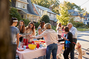 Neighbours talk standing around a table at a block party