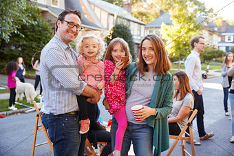 Parents holding young kids smile to camera at a block party
