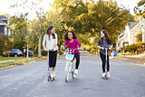 Three pre-teen girls riding in street on scooters and a bike
