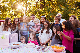 Young girl blowing out candles at her birthday garden party