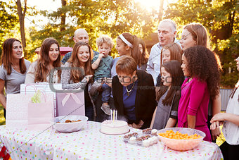 Senior woman blows out candles at her birthday garden party