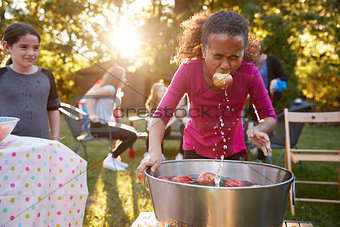 Pre-teen girl, apple in mouth, apple bobbing at garden party