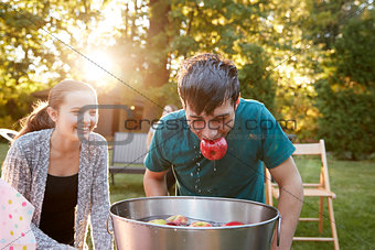 Teenage boy, apple in mouth, apple bobbing at garden party