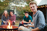 Teenage boy with friends toasting marshmallow at a fire pit