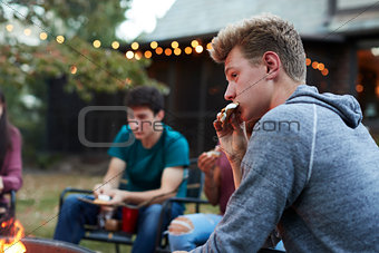 Teenage boy eating sÕmore with friends at a fire pit