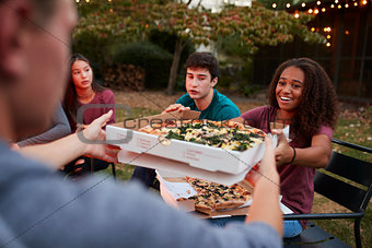 Teenage friends sitting at fire pit sharing take-away pizzas