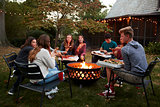 Teenage friends sit round a fire pit eating take-away pizza