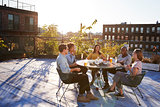Five friends sit talking at a table on a New York rooftop