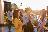 Female friends talking at a rooftop party, backlit