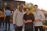 Three male friends at a rooftop party smiling to camera