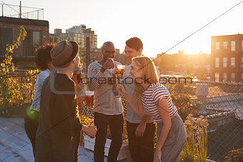 Friends stand talking at rooftop party, backlit by sunlight