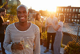 Young man holding glass at a rooftop party smiling to camera