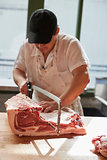 Young butcher sawing meat at a butcher's shop, vertical