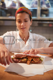 Young woman wrapping a sandwich at a deli counter, vertical