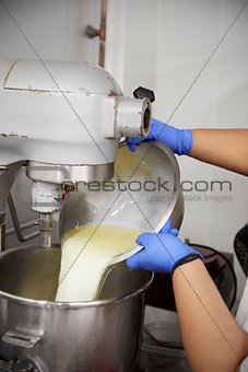 Woman pouring cake mix into a large mixing bowl at a bakery