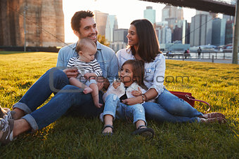 Young family with two daughters sitting on lawn, close up