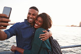 Young black couple taking photo on quayside, front view
