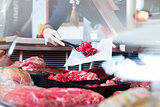 Meat in a butcher shop display being put in by sales woman