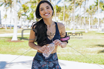 Relaxing sportswoman with bottle of water in park